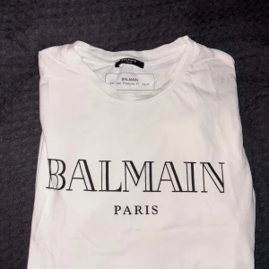 Vit Balmain Paris t-shirt  - Vit t-shirt från Balmain Paris med klassisk svart logotyp framtill. T-shirten är använd men inte så att det syns. Det är förövrigt jätteskön och passar till alla mina outfits. Men den sitter lite för litet på mig nu så jag säljer vidare den!