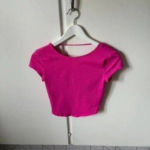 Rosa croppad topp från SHEIN BAE - Säljer en knallrosa croppad topp från SHEIN BAE i storlek XS. Toppen har korta ärmar, rund halsringning och en öppen rygg med en smal rem upptill. Perfekt för dig som gillar färgstarka och trendiga plagg.