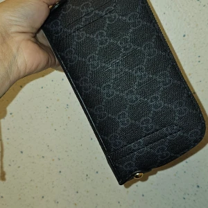 Svart plånbok från Ggggi med monogram - Snygg svart plånbok från Gi med klassiskt G-monogram över hela ytan. Plånboken har dragkedja i guldton och flera fack för kort och sedlar. Tillverkad i slitstarkt material med läderdetaljer, perfekt för dig som gillar lyxiga accessoarer.Betala med direkt swish far du gratis frakt:)