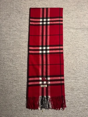 Rutig röd Burberry kashmirväst - Snygg rutig väst från Burberry i rött, svart och vitt med klassiskt mönster och fransar längst ner. Västen är tillverkad i 100% kashmir och har en broderad Burberry-logga framtill. Perfekt för dig som gillar lyxiga och tidlösa plagg.