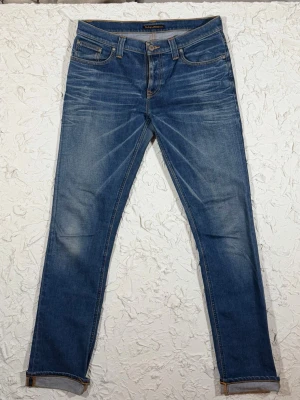  Nudie Jeans - tube Kelly  - Snygga blå jeans från Nudie Jeans med skinny passform och klassisk femficksdesign. Jeansen har orangea kontrastsömmar och coola slitningar framtill och på baksidan. Materialet är jeans med en mjuk känsla och detaljer som logopatch och broderade bakfickor.