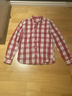 Rutig röd skjorta från Levi's - Säljer en snygg rutig skjorta från Levi's i rött och vitt. Skjortan har klassisk krage, långa ärmar och knappar framtill. Standard fit och tillverkad i mjuk bomull. Perfekt för dig som gillar avslappnad stil med lite edge.