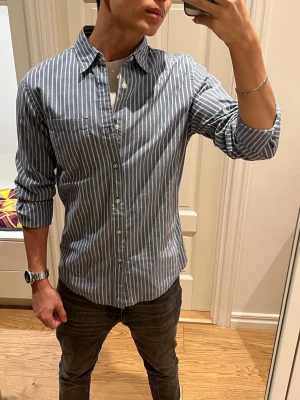 Randig blå skjorta från Sonoma - Snygg blå skjorta från Sonoma med vita  ränder och klassisk krage. Tillverkad i mjuk bomull. Perfekt för dig som gillar stilrena och fräscha plagg. Inga defekter. Hör av dig vid minsta fråga👋