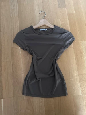 Brun t-shirt från 157, storlek S - Säljer en enkel brun t-shirt från 157 i storlek S. T-shirten har rund hals och korta ärmar, med en slät och mjuk yta som känns skön mot huden. Perfekt för dig som gillar stilrena och neutrala plagg. Materialet är troligtvis polyester.