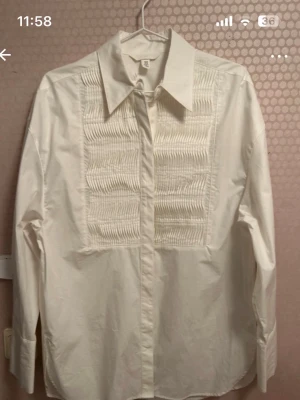 Vit skjorta med plisserad detalj H&M XS - Klassisk vit skjorta från H&M i storlek XS med snygga plisserade detaljer framtill. Skjortan har lång ärm, bred krage och knäppning framtill och passar även stl S. 