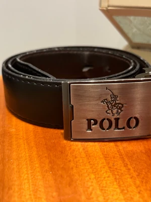 Svart läder skärp från ralph lauren  - Snyggt svart skärp från Polo Ralph Lauren med en stilren metallspänne där Polo-loggan är ingraverad. Skärpet är gjort i slätt skinn och har klassisk design som passar till jeans eller kostymbyxor. Perfekt accessoar för att lyfta din outfit. Finns tecken av användning men påverkar inte användningen, det syns inte.