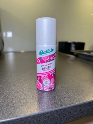 Batiste Blush Dry Shampoo 50ml - Batiste Blush flirty floral torrschampo i en smidig 50ml sprayflaska med vit kork och rosa blommigt mönster. Doften är flirty floral och produkten fräschar upp håret utan att torka ut. Perfekt att ha med i väskan för snabb uppfräschning mellan tvättar.