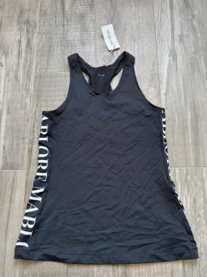 Svart fitness linnetopp från Mablore - Säljer en svart fitness linnetopp från Mablore i storlek S. Toppen har breda axelband och racerback-design, med vit text längs sidorna. Materialet är mjukt och stretchigt, perfekt för träning. Snygg och sportig look med stilren logga.