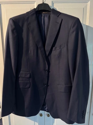 Rose & Born x Loro piana  - Snygg mörkblå kavaj från Rose & Born, tillverkad i Italien. Klassisk modell med två knappar, flera fickor och helfodrad insida. Materialet är ull och kavajen har långärmade ärmar med knappdetaljer vid mudden. Perfekt för dig som vill ha en stilren look. Loro piana tyg, nypris 15000. #loro piana, #brunello cucinelli, Rose & Born 