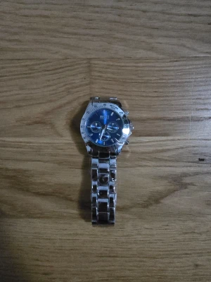 Silvrig Hugo Boss klocka blå urtavla - Klocka från Hugo Boss med blå urtavla och silverfärgat armband. Helt ny med plast på. För ett väldigt billigt pris.