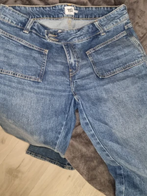 Blå jeans från 157 med utsvängda ben - Säljer ett par klassiska blå jeans från 157 med utsvängda ben och stora fickor både fram och bak. Jeansen har låg  midja och är tillverkade i slitstarkt denimtyg. Perfekt för dig som gillar enkel och tidlös stil. Passar till sneakers eller boots.