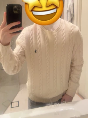 Vit stickad tröja från Polo Ralph Lauren - Säljer en vit kabelstickad tröja från Polo Ralph Lauren med klassisk rund hals och ribbade muddar. Tröjan har det ikoniska Polo-logot broderat på bröstet och är tillverkad i mjuk bomull. Perfekt för dig som gillar stilrena och tidlösa plagg. Vid snabb affär så kan priset rabatteras.