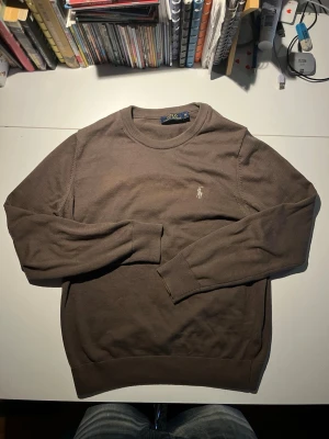 Brun tröja från Polo Ralph Lauren - Säljer en brun långärmad tröja från Polo Ralph Lauren i storlek S. Tröjan har rund hals, ribbade muddar och en liten broderad logga på bröstet. Tillverkad i 100% bomull, perfekt för dig som gillar klassisk och enkel stil.