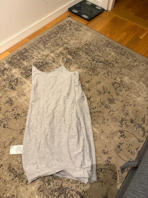 Ljusgrå linnetopp med smala axelband - Säljer en ljusgrå linneklänninh  med smala axelband och enkel design. Toppen är ärmlös och har en mjuk, stretchig känsla i bomullsmaterial. Perfekt för varma dagar eller som lager under andra plagg.