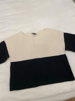 Beige och svart ribbad topp från Lindex - Säljer en stilren topp från Lindex i storlek S. Toppen är ribbad och har en beige överdel med svart nedre del och svarta ärmar. Modellen är rak och har rund hals. Perfekt för dig som gillar enkla färgblock och mjuka material.