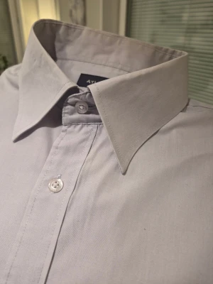 Ljusgrå skjorta från Atlant XL - Snygg ljusgrå skjorta från Atlant i storlek XL. Klassisk modell med lång ärm, bröstficka och knappar framtill. Skjortan har en stilren krage och är gjord i mjuk bomull som känns skön mot huden. Perfekt för dig som gillar enkel och clean stil.