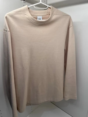 Beige långärmad tröja från Zara - Snygg beige långärmad tröja från Zara med enkel och stilren design. Passar perfekt för något vardagligt eller ha den över ryggen tillsammans med en skjorta. Den är i mycket bra skick och är knappt amvänd.