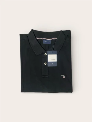 Svart pikétröja från GANT - Säljer en svart oanvänd pikétröja från GANT med klassisk krage och två vita knappar framtill. Tröjan har broderad GANT-logga med sköld på bröstet och är tillverkad i mjuk bomull. Perfekt för en clean och stilren look.