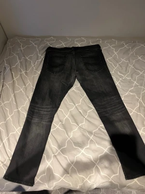 Svarta jeans från Jack & Jones - Snygga svarta jeans från Jack & Jones med klassisk femficksdesign och diskreta slitningar på benen. Jeansen har rak passform och är tillverkade i slitstarkt bomullsmaterial med lite stretch för extra komfort. Perfekta för dig som gillar en enkel och stilren look.