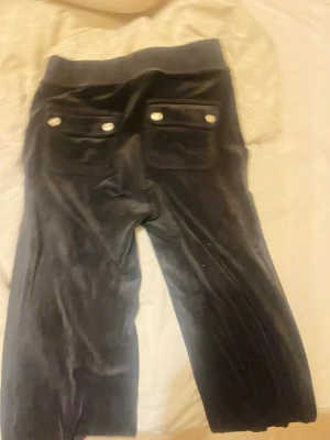 Juice byxor  - Säljer en svart väst i mjuk manchester med bred resår upptill och två fickor bak med silvriga knappar. Västen har en klassisk rak form och passar perfekt för dig som gillar stilrena detaljer och vill ha något som sticker ut lite extra.