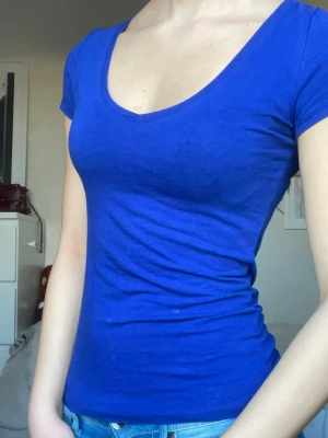 Söt V-ringad topp - Säljer en blå t-shirt från H&M i storlek XS. T-shirten har v-ringad hals, korta ärmar och är figurnära i passformen