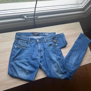 Replay Anbass - Snygga blå Replay Anbass jeans med klassisk femficksdesign och diskreta slitningar. Jeansen har raka ben, slim passform och är tillverkade i mjukt jeanstyg med stretch. Perfekt för dig som gillar stilrena och bekväma jeans med coola detaljer. Storlek 30/32