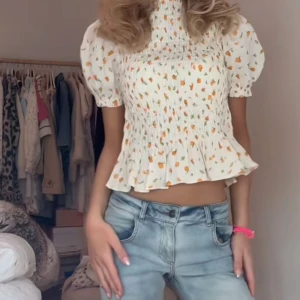 Vit blommig blus med puffärm - Supersöt vit blus med små orange blommor och gröna blad, puffärmar och smockad överdel. Blusen har volang nertill. 🍊🤍