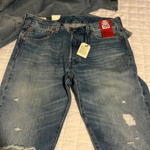 Levi's 501 jeans blå 34x32 - Säljer ett par klassiska Levi's 501 jeans i blå tvätt med slitna detaljer och raka ben. Jeansen har fem fickor, knappgylf och den ikoniska läderpatchen bak. Perfekt för dig som gillar en tidlös och avslappnad look.