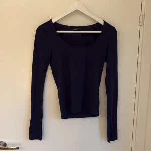 Mörkblå långärmad topp från Gina Tricot - Säljer en stilren mörkblå långärmad topp från Gina Tricot. Toppen har en djup rundad halsringning och är figurnära i modellen. Perfekt att styla med jeans eller kjol för en enkel och snygg look.