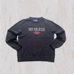 Svart stickad tröja Morris Co M - Svart stickad tröja från Morris Co i storlek medium. Tröjan har broderad logga och Union Jack-flagga framtill, samt ribbade muddar vid ärmslut och nederkant. Klassisk rund halsringning och långärmad modell, perfekt för dig som gillar stilrena detaljer.