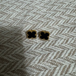 Svart-guldiga clover örhängen - Snygga örhängen i fyrklöverform med svart mitt och guldfärgad kant. De har en elegant och trendig look med detaljerade kanter som ger extra lyxkänsla. Perfekta för att lyfta vilken outfit som helst.