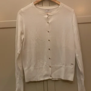 Vit kofta från Holly & Whyte Lindex M - Klassisk vit kofta från Holly & Whyte by Lindex i storlek M. Koftan har rund halsringning, långa ärmar och knäppning med guldiga knappar framtill. 