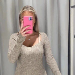 Beige ribbad stickad klänning - Säljer en beige stickad klänning med ribbad struktur och långärmad design. Klänningen har en snygg v-ringad hals och sitter figurnära. Perfekt för dig som gillar en enkel men stilren look.