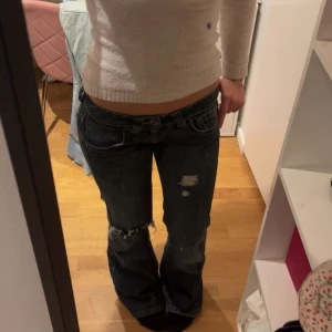 mörkblå lågmidjade jeans - Säljer ett par jeans i mörkblå tvätt med slitningar och hål på knät. Lågmidjade med bootcut passform. Perfekt för dig som gillar en avslappnad och cool stil.
