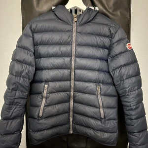 Mörkblå dunjacka från Colmar - Snygg mörkblå dunjacka från Colmar med huva och två dragkedjeförsedda fickor. Jackan har quiltad design och Colmar-logga på ärmen. Perfekt för kyliga dagar och har en clean, sportig look. Har ett mindre hål vid handleden skickar bild vid intresse. Storlek 46 alltså small. Tveka inte på att skriva vid frågor.