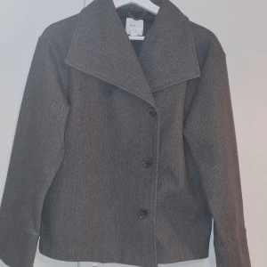 Grå kappa från Gina Tricot - Stilren grå jacka från Gina Tricot. Jackan har rak passform och långa ärmar, perfekt för kyliga dagar. Enkel och snygg design som passar till det mesta.