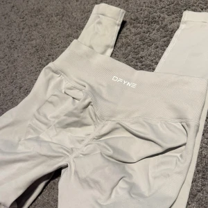 Grå leggings från DFYNE, storlek S - Snygga ljusgrå leggings från DFYNE med hög midja och ribbad linning. Tillverkade i ett stretchigt material av 90% nylon och 10% elastan. Diskret logga framtill och sömlös design.