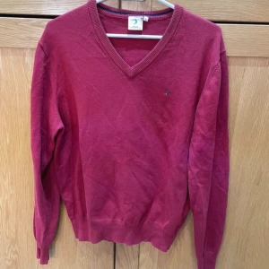 Vinröd v-ringad tröja från Boomerang - Vinröd v-ringad tröja från Boomerang med liten broderad logga på bröstet. Tröjan har långa ärmar, ribbade muddar och är tillverkad i mjuk bomull. Perfekt för dig som gillar klassisk och stilren look.