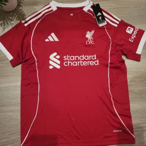 Liverpool FC röd matchtröja Adidas S - Liverpool FCs officiella matchtröja från Adidas från 2025/26. Tröjan har korta ärmar och är tillverkad i lätt, ventilerande polyester med Aeroready-teknologi. Snygga vita ränder på axlarna och broderad klubbmärke på bröstet.