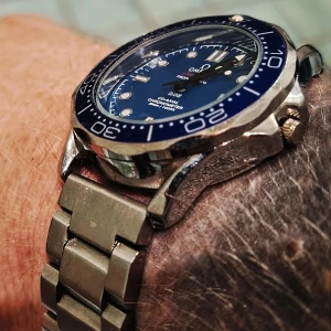 Omg Sea master Pro blå vågor custom stålarmband - Säljer en Omega Seamaster Professional med blå urtavla och matchande blå bezel. Klockan har ett robust stålarmband och vågmönster på urtavlan. Snygga lysande index och datumfunktion vid kl 6. Perfekt för dig som gillar klassisk och sportig stil.