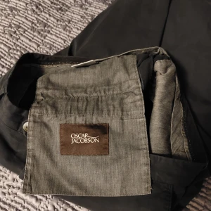 Kostymbyxor Oscar Jacobson svarta  - Snygga svarta kostymbyxor från Oscar Jacobson i klassisk rak modell. Byxorna har sidfickor, hällor för bälte och två bakfickor med knapp. Perfekta för en stilren look och tillverkade i ett mjukt bomullstyg. Storlek 50. Köpte de för strax under 2000kr.