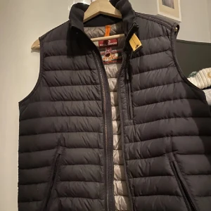 Svart dunväst från Parajumpers M - Våga buda! Snygg svart dunväst från Parajumpers i storlek M. Västen är quiltad med horisontella sömmar och har en hög krage samt dragkedja framtill. Insidan är grå och har coola detaljer som etikett med 'Super Lightweight'. Perfekt för lager-på-lager och streetstyle. Scannen tar dig till deras hemsida!