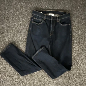 Mörkblå jeans från Vailent - Snygga mörkblå jeans från Vailent med klassisk femficksdesign och kontrastsömmar. Modellen har rak passform och normal midja, tillverkade i slitstarkt denimtyg. Perfekta för dig som gillar stilrena och tidlösa jeans. Lite sönder på högra benet se på bild 2.