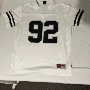 Dunder tränings tröja  - Snygg vit fotbollströja från Reckless med svart tryck av nummer 92 på både fram- och baksidan. Tröjan har svarta ränder på ärmarna och ett klassiskt sportigt snitt med V-ringad krage. Materialet är mesh för extra ventilation och komfort. Kan även passa mindre L 