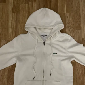Vit Lacoste hoodie Small - Stilren vit zip hoodie från Lacoste i storlek Small, jätte bra passform och sitter snyggt på, skickar paket inom 1 timme 