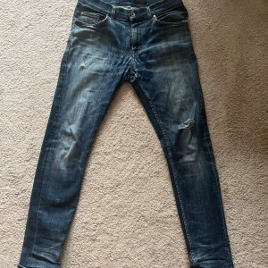 Mörkblå skinny jeans med slitning Tiger of Sweden - Snygga mörkblå jeans med skinny passform och slitning på ena benet. Klassisk femficksmodell med dragkedja och knapp framtill. Jeansen har en tvättad look och är perfekta för en avslappnad stil.