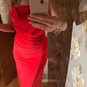 Röd långklänning från Zara - Säljer en snygg röd långklänning från Zara med draperad halsringning och smickrande rynkade detaljer längs sidan. Klänningen är ärmlös och har en figurnära passform som framhäver siluetten. Perfekt för dig som vill sticka ut med en färgstark look.