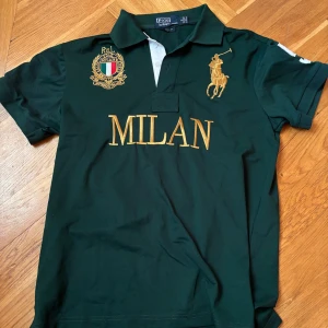 Grön Polo Ralph Lauren Milan piké - Snygg grön pikétröja från Polo Ralph Lauren med gul broderad MILAN-text och emblem på bröstet. Klassisk krage, korta ärmar och ikonisk polospelare i guld. Materialet är mjuk bomull och passformen är custom fit. Perfekt för dig som gillar sportig och stilren look. Säljer den för att jag växt ut den men den är endast använd vid ett tillfälle av mig då den var lite liten redan när jag köpte den och priset är pågrund av att den är köpt på plick därför ett riktigt bra pris,,, Först till Kvarn  💪💪