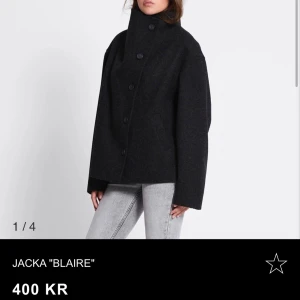 Svart ulljacka med hög krage - Stilren svart jacka i ull med hög krage och knäppning framtill. Jackan har en loose passform, raka axlar och långa ärmar. Perfekt för dig som gillar minimalistisk och clean stil.