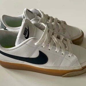 Vita Nike sneakers med gummisula - Snygga vita Nike sneakers med svart swoosh och klassisk gummisula. Skorna har snörning, rund tå och är tillverkade i syntet och skinn. 